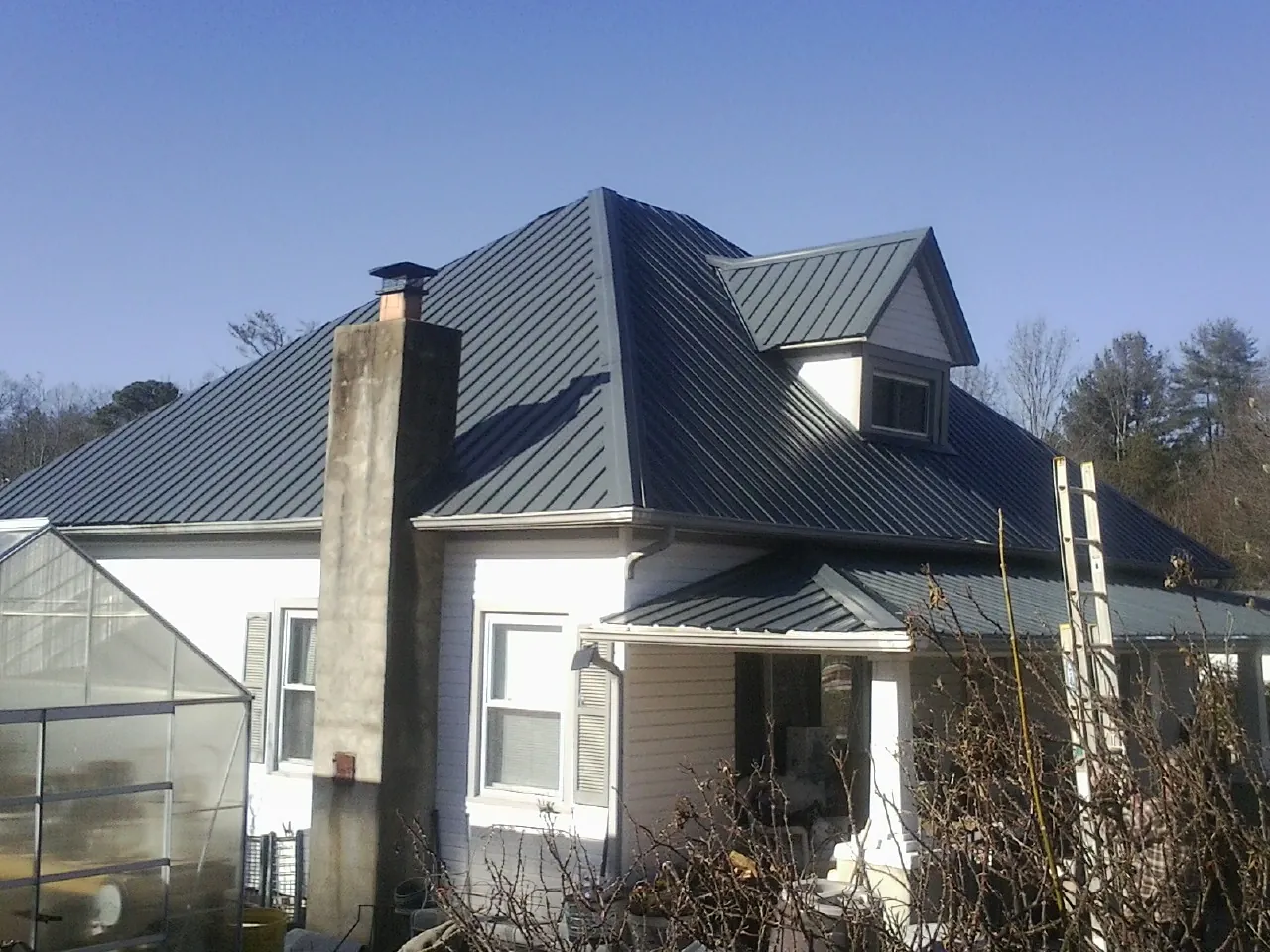 Dark blue standing seam metal roof on a white farmhouse with dormer — Slate & Tile Roof Repair by Roofing Brothers in Balsam Grove