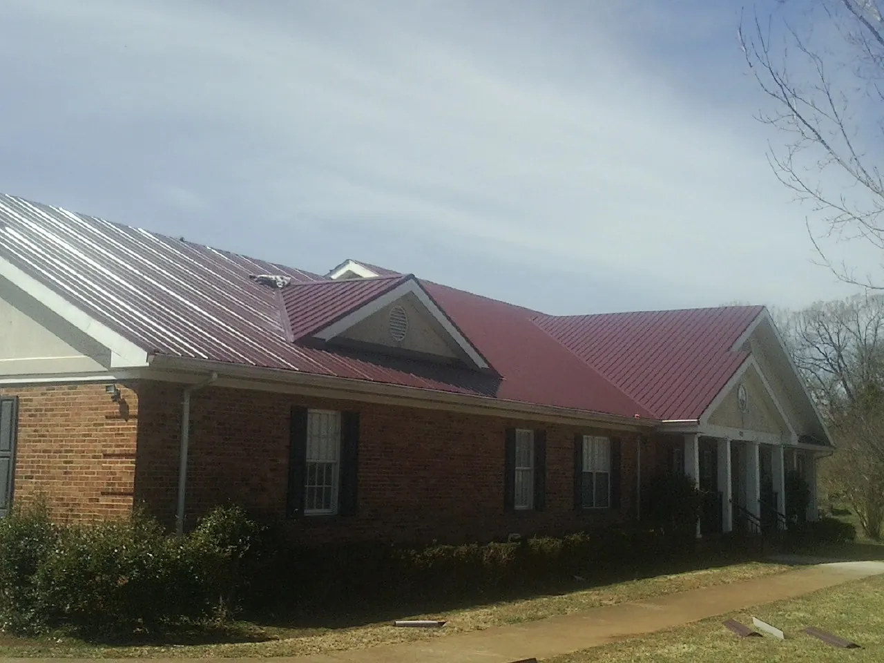Red metal roof with gabled entries on a long brick building, from a Hail Damage Roof Repair job in Balsam Grove