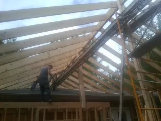 Rafters going up over a new addition with a worker on the wall in Balsam Grove