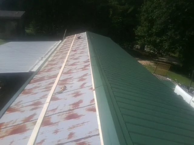Old rusted panels beside newly installed green metal roofing — Wind Damage Roof Repair by Roofing Brothers in Balsam Grove