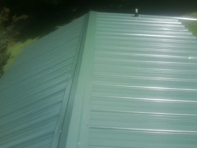New green metal panels meeting at the ridge of a roof — Flat Roof Repair work by our crew in Balsam Grove