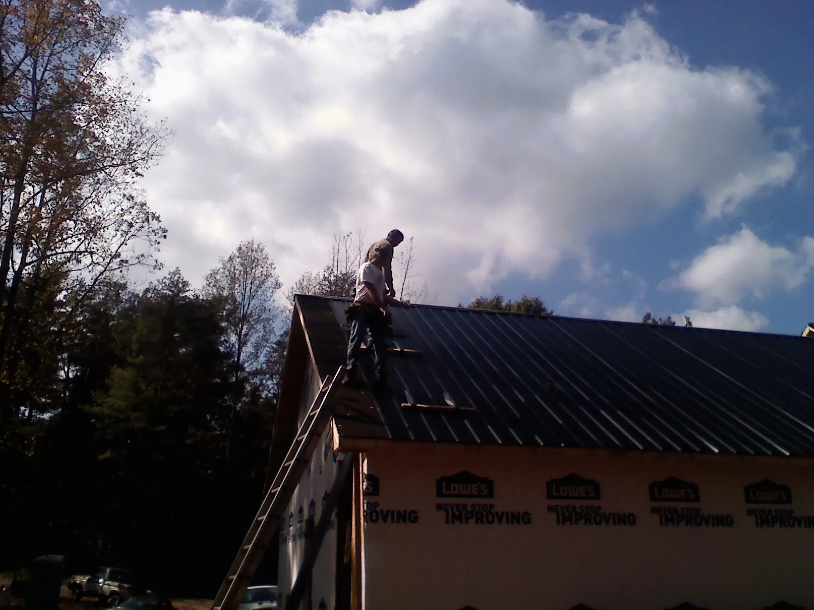 Roofer fastening dark metal panels high against a cloudy sky, from a Roof Inspection job in Balsam Grove