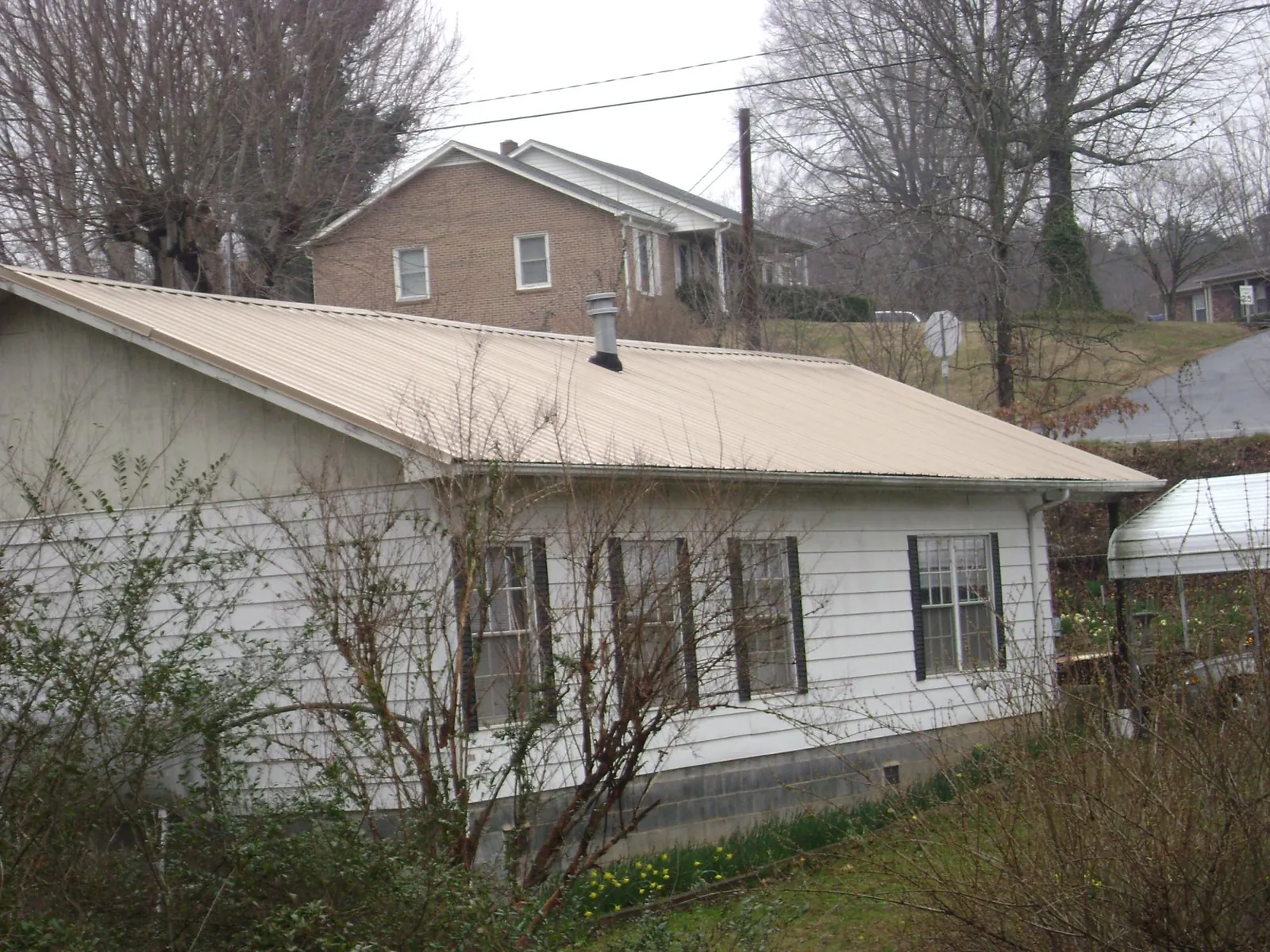 Tan metal roof on a white sided house set into a hillside — Commercial Roofing by Roofing Brothers in Balsam Grove