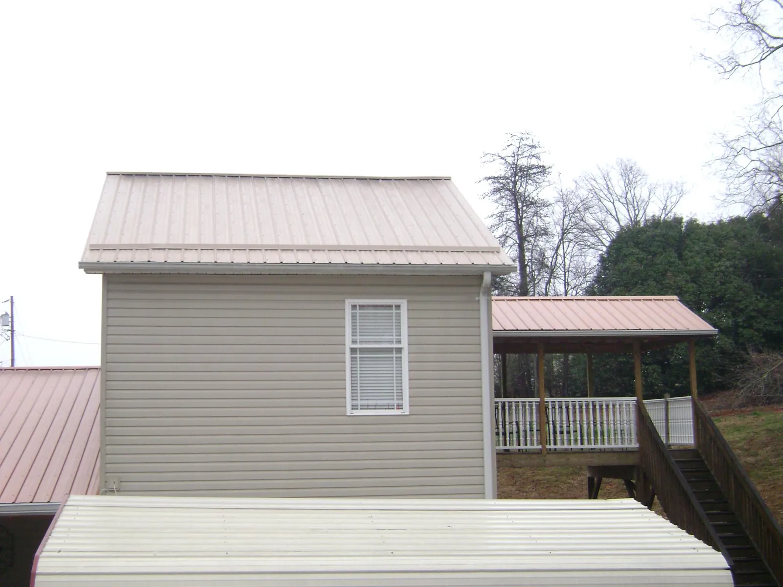 Tan metal roofs on a two story addition and attached porch, from a Roof Replacement job in Balsam Grove